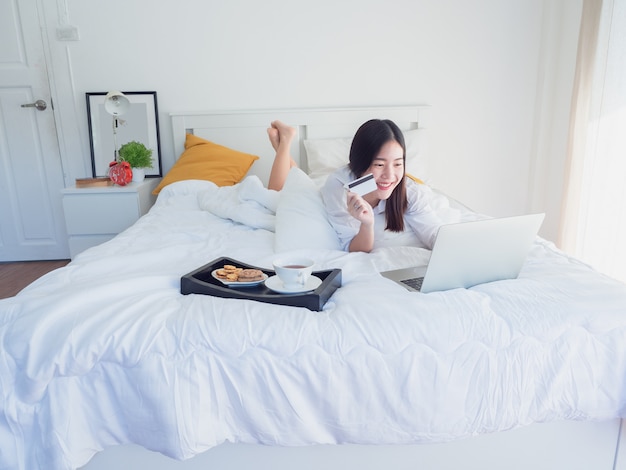 Asian girl using computer with credit card on bed