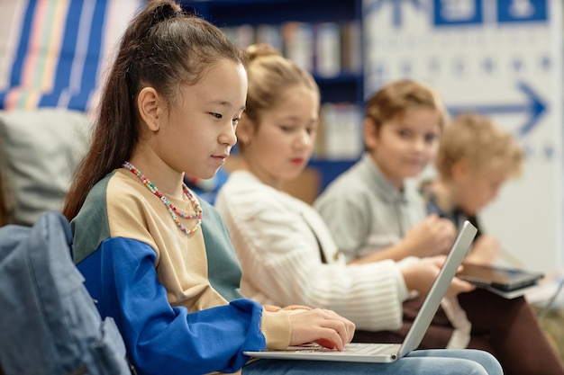 Asian girl using laptop in library with children in background