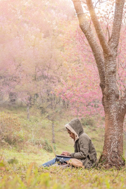 Ragazza asiatica che utilizza un computer portatile sotto l'albero