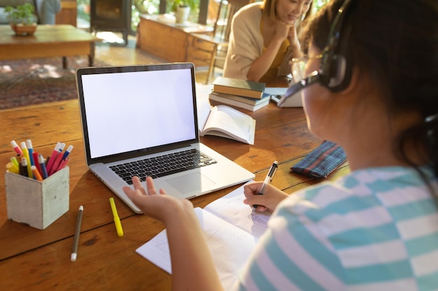 Asian girl using laptop with blank screen, writing, learning online her mum working in background