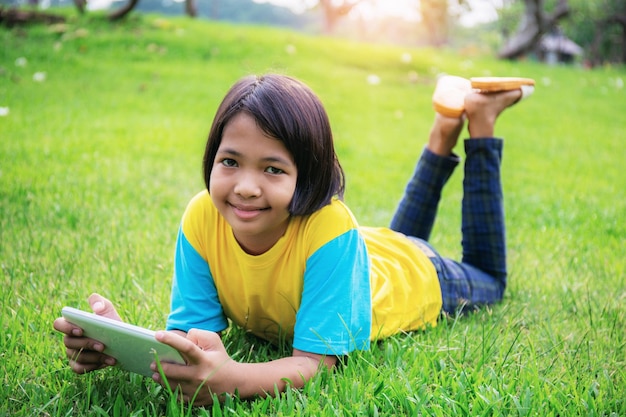 Ragazza asiatica utilizzando tablet sul prato