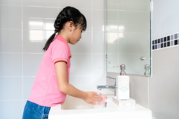 Asian girl washing hands with soap under the faucet with water in bathroom at home