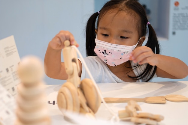 아시아 소녀는 코로나 바이러스 2019 (covid-19)를 예방하기 위해 마스크를 쓰고 학교에서 장난감을 가지고 놀아요.