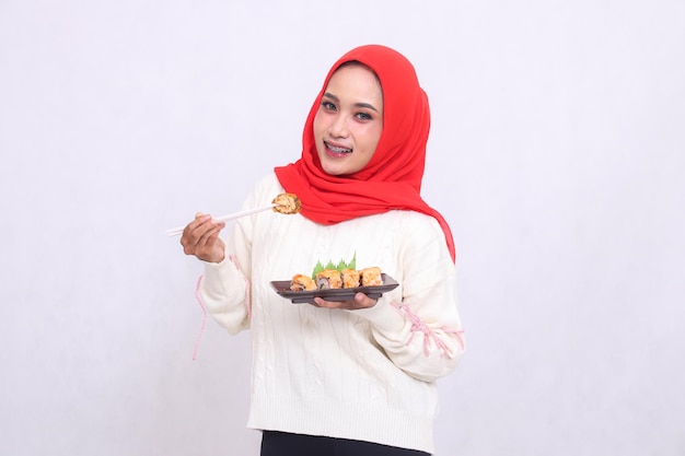 Азиатская девушка в хиджабе весела для камеры, поднимает палочки и носит тарелку.