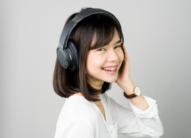 Asian girl in white casual dress listening to music from black headphones.