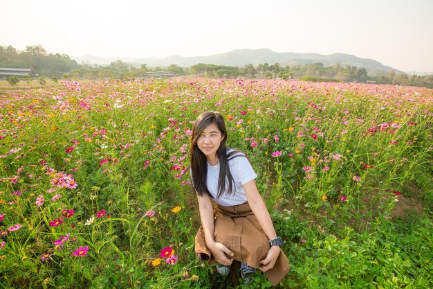 白いドレスを着たアジアの女の子は、コピーで夏の田舎のピンクの花の牧草地に座っています