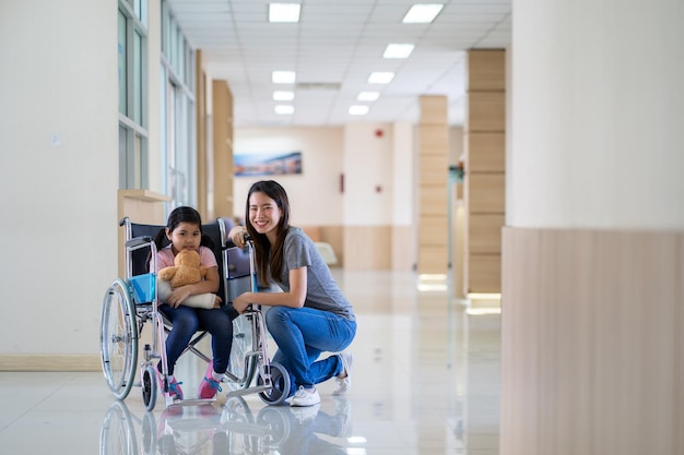 Ragazza asiatica con un braccio rotto che indossa un cast su sedia a rotelle con sua madre in ospedale