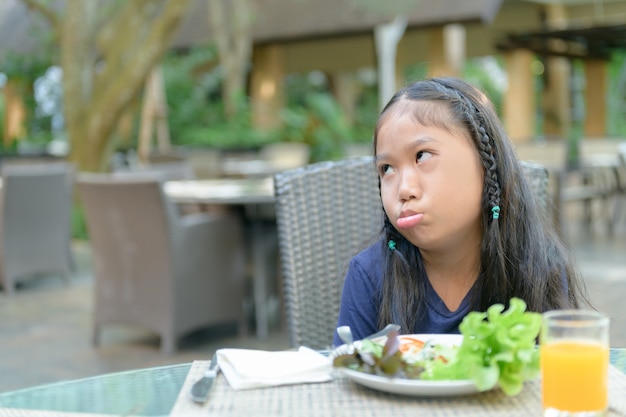 Asian girl with expression of disgust against vegetables 