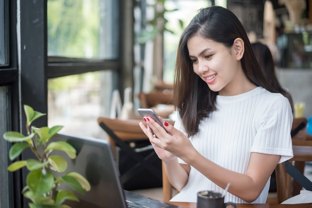 ラップトップとスマートフォンを持つカフェで働くアジアの女の子