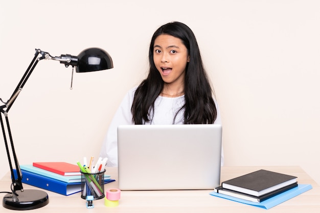 Asian girl in a workplace with a laptop on beige wall with surprised facial expression