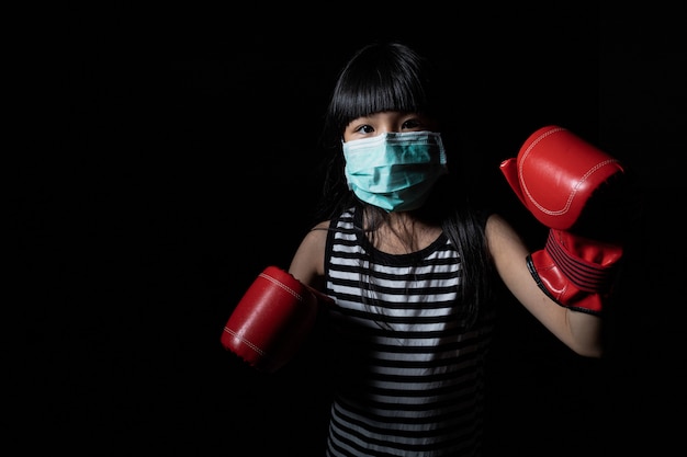 写真 アジアの女の子はウイルスから保護するためにフェイスマスクを着用し、ウイルスとの闘いをコロナウイルスとして象徴するボクシンググローブを着用します