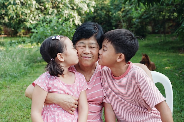 Asian grandchildren kissing their grandmother in the park, Happy Asian senior woman