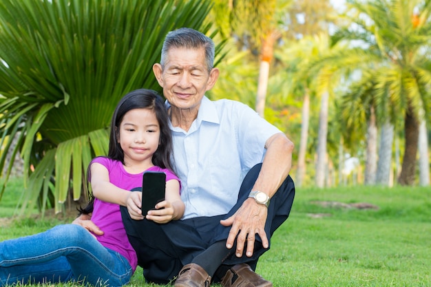 アジアの祖父と孫が公園でスマートフォンでselfieを取る