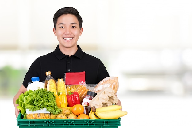 An Asian grocery store delivery man wearing a black poloshirt holding food basket