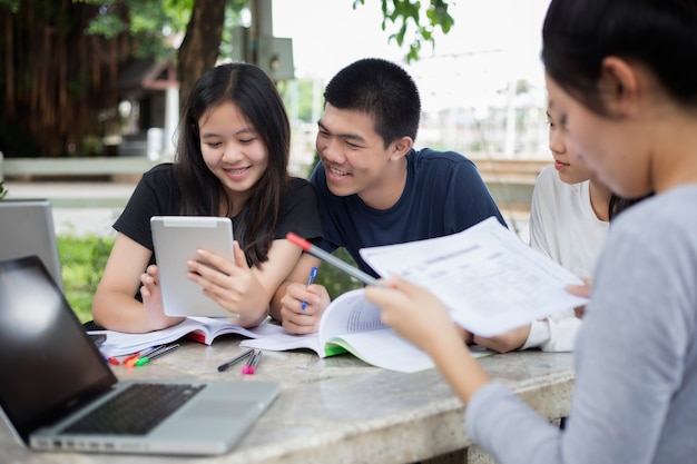 Asian Group of students using tablet and notebook sharing with the ideas for working on the campus l