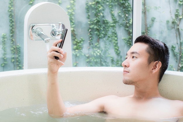 Photo asian guy in bathtub and look smartphone