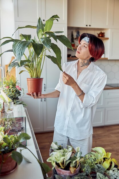 Photo asian guy holding large flowerpot and touching the leaves with his hands