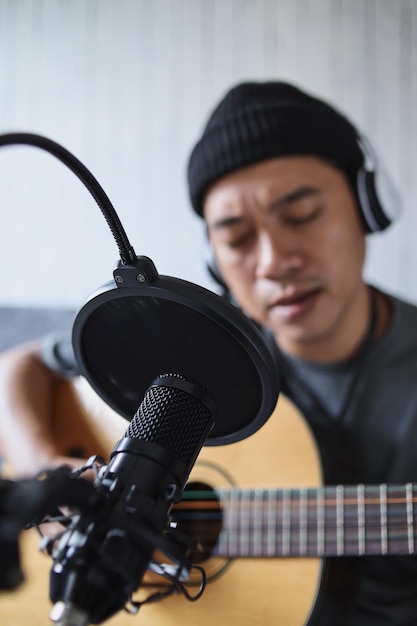 Ragazzo asiatico che suona il podcast audio di registrazione della chitarra in studio usando il microfono. persone e musica co