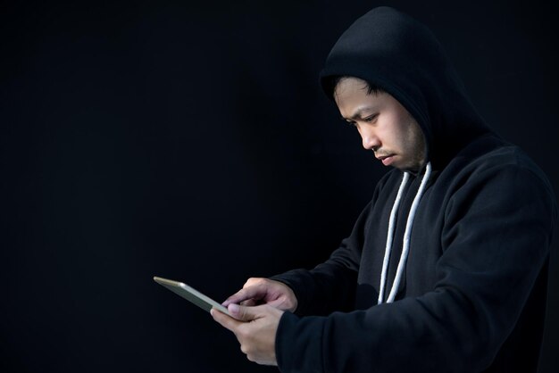 Asian hacker in black hood on black backgroundHack passwordhacking safety systems to steal information