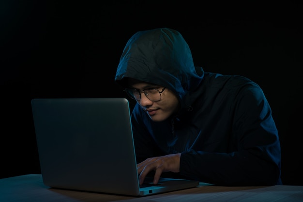 Asian hacker hacking computer network with laptop in dark. Cyber security concept