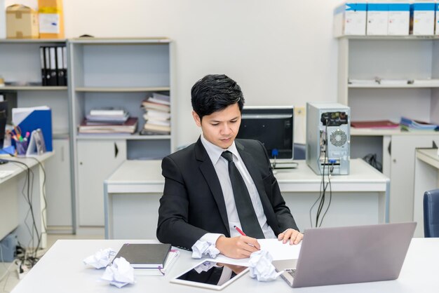 Asian handsome Businessman in suit work hard with crumped paper in the officeYoung man stressed about the declining sales of the company