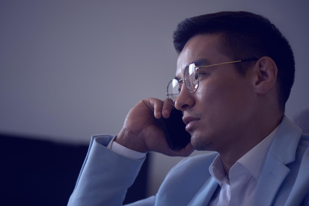 정장과 안경을 쓴 아시아의 잘생긴 카자흐 사업가가 사무실에서 일하고, 성공적인 전문 경영인은 휴대전화로 비즈니스 문제를 해결합니다