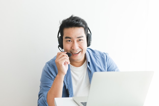 Asian handsome man in blue shirt using laptop with headphone talking smile and happy face