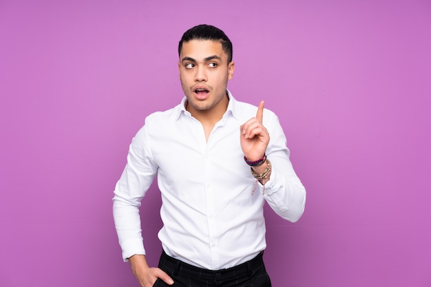 Asian handsome man on blue wall thinking an idea pointing the finger up