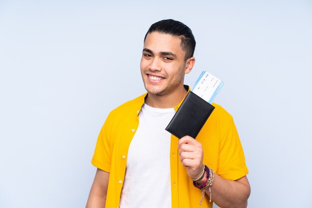 Asian handsome man isolated on blue wall happy in vacation with passport and plane tickets