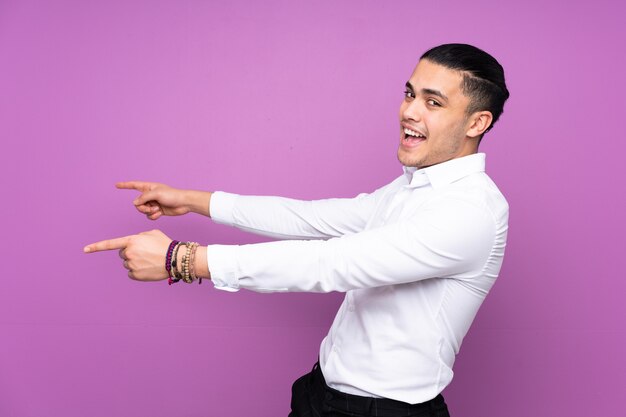 Asian handsome man isolated on blue wall pointing finger to the side and presenting a product