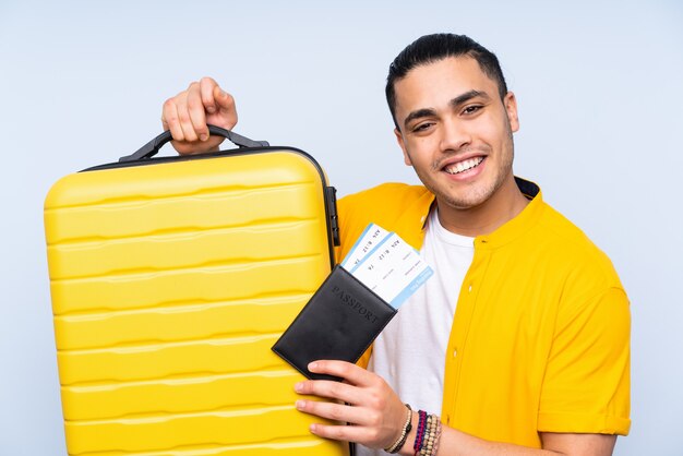 Asian handsome man isolated on blue wall in vacation with suitcase and passport