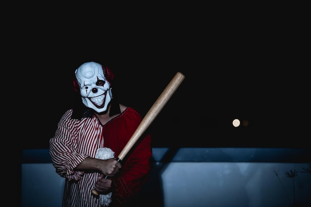 아시아 잘 생긴 남자는 밤 장면에서 무기로 광대 마스크를 착용할로윈 축제 개념주황색 옷을 입은 살인자의 무서운 무서운 사진사악한 광대 캐릭터