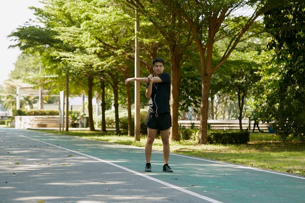 アジアのハンサムな男性は、朝、公園を歩いたりジョギングしたりする前にウォームアップします。