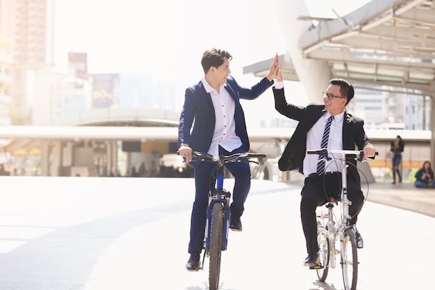 Asian handsome young businessmen talking while riding bicycles in city