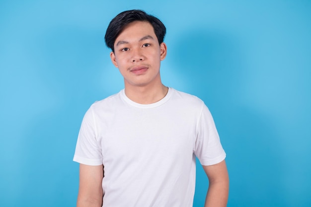 Asian handsome young man standing wears white tshirtwith he looking to camera on blue background