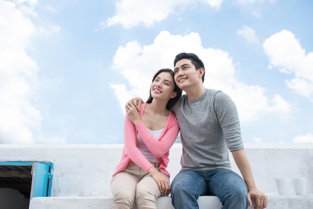 Asian happy couple sitting together over sky blue