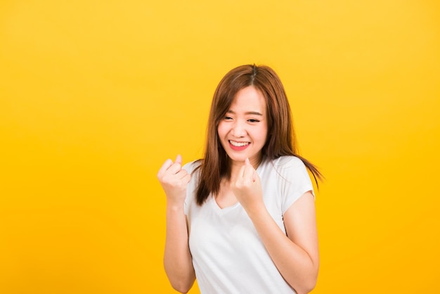 Asian happy portrait beautiful cute young woman teen standing wear t-shirt makes raised fists up celebrating her success looking to camera isolated, studio shot on yellow background with copy space