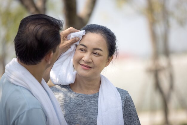 屋外公園で走った後、妻の顔から汗を拭くアジアの幸せな年配のカップルの夫。