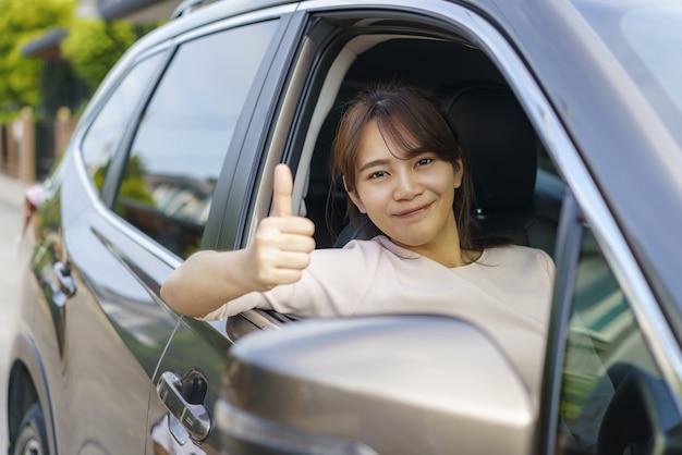 Asian happy young beautiful woman driving a car and thumb up