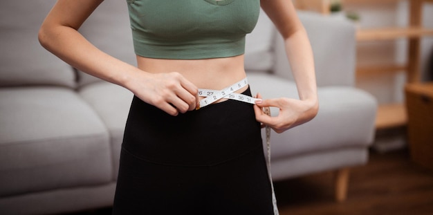 Asian healthy woman dieting Weight loss Slim woman measuring waist with measure tape after diet at home weight control