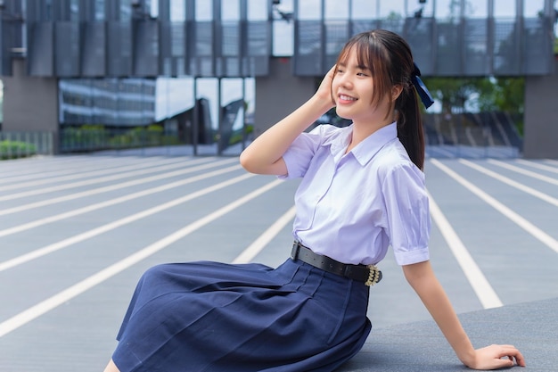 自信を持って建物を背景に笑顔で学校の制服を着たアジアの高校生の女の子