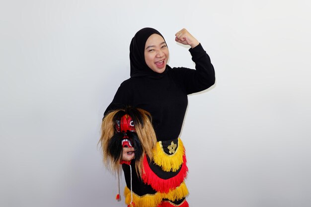 Asian hijab woman holding a Jatilan mask while screaming and clenched fist isolated on white background