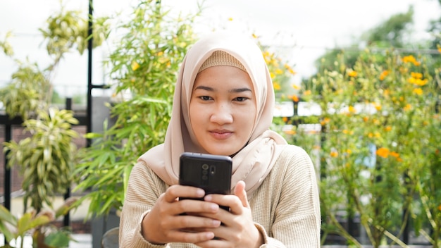 Donna asiatica hijab che gioca telefono al caffè