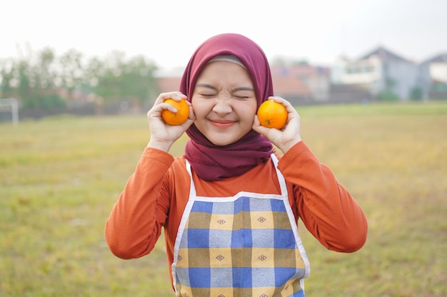 Asian hijab woman wearing apron holding an orange fruits