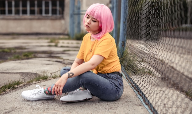 Asian hipster sitting on city street