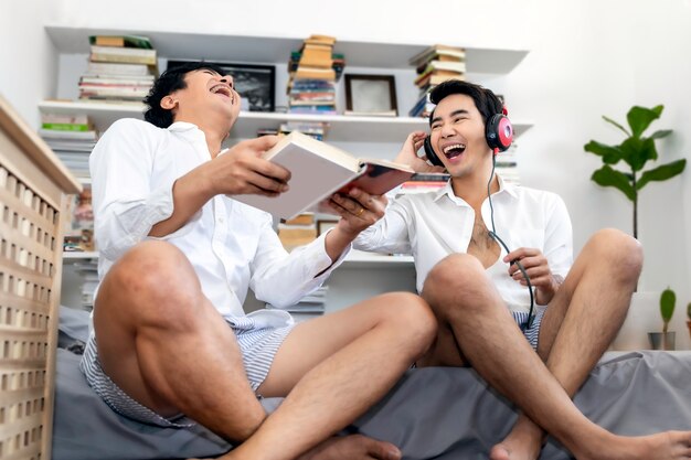 Asian homosexual couple laugh and listen to music sitting in home living room