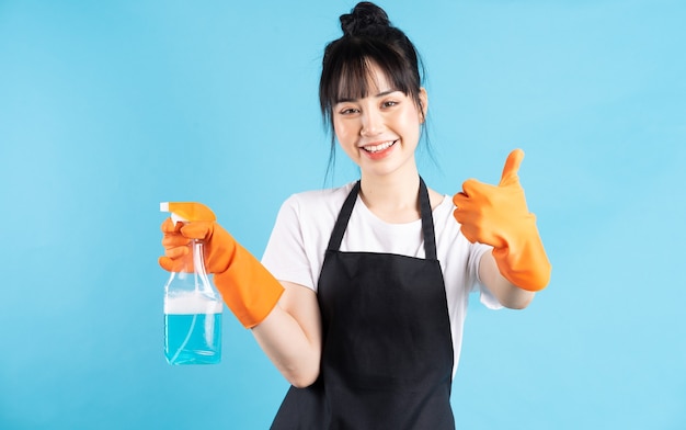 Азиатская домохозяйка в оранжевых перчатках держит в руке струю воды
