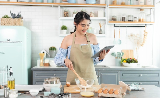 Casalinga asiatica in cucina utilizzando tablet per la ricerca di ricette online cucinare pasta da forno fatta in casa