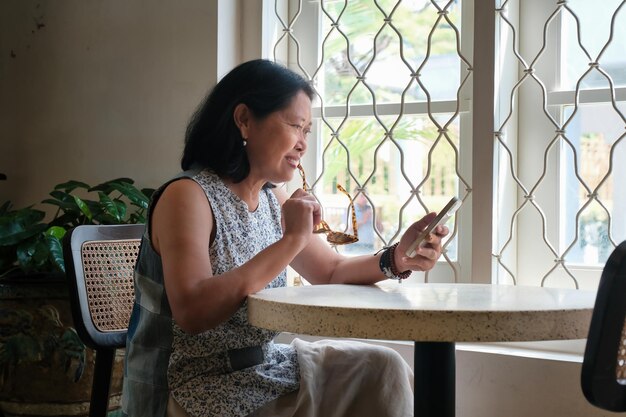 Photo asian housewife looking happy reading message from her smartphone in the house