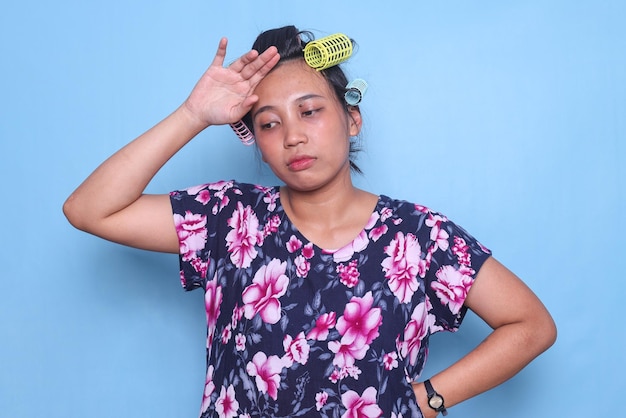 Asian housewife with hair curlers touching her head feeling tired and suffering from migraine